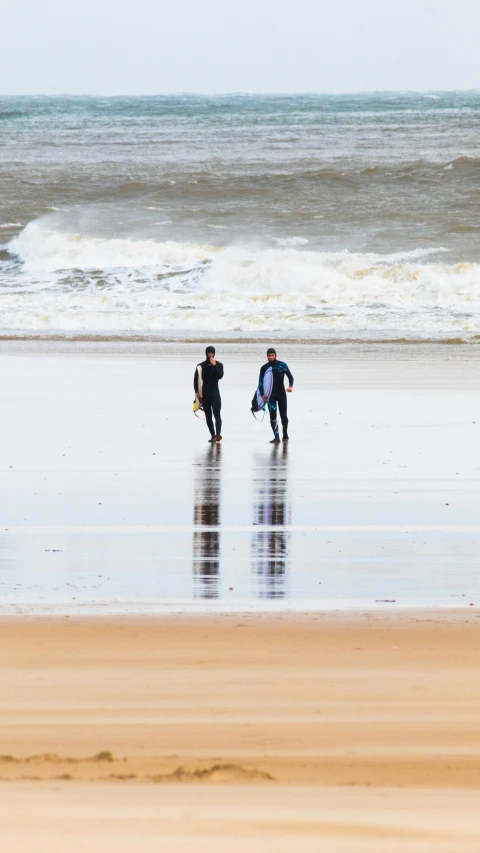 two people walking on beach next to water