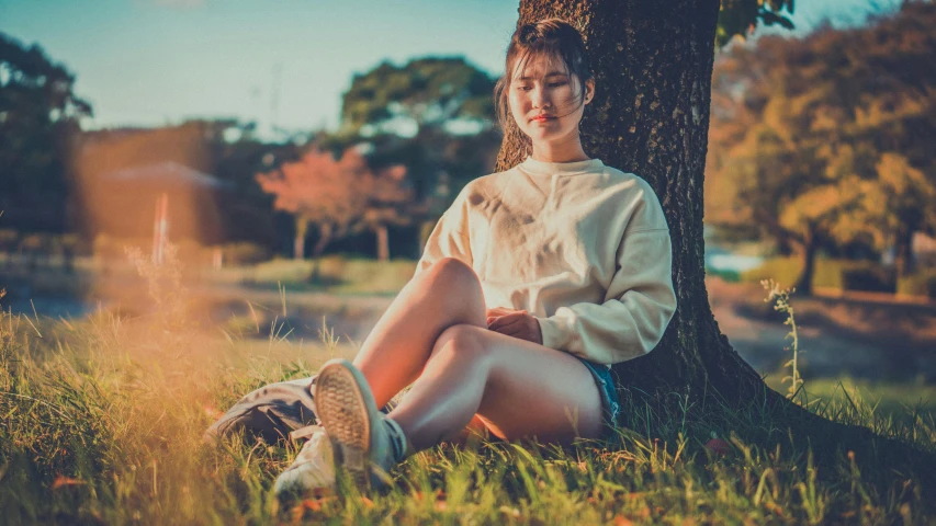 a woman sitting on the grass near a tree with her feet up