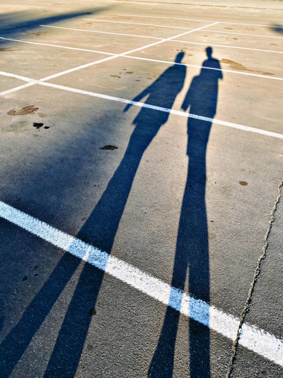 the shadows of two people on an asphalt parking lot