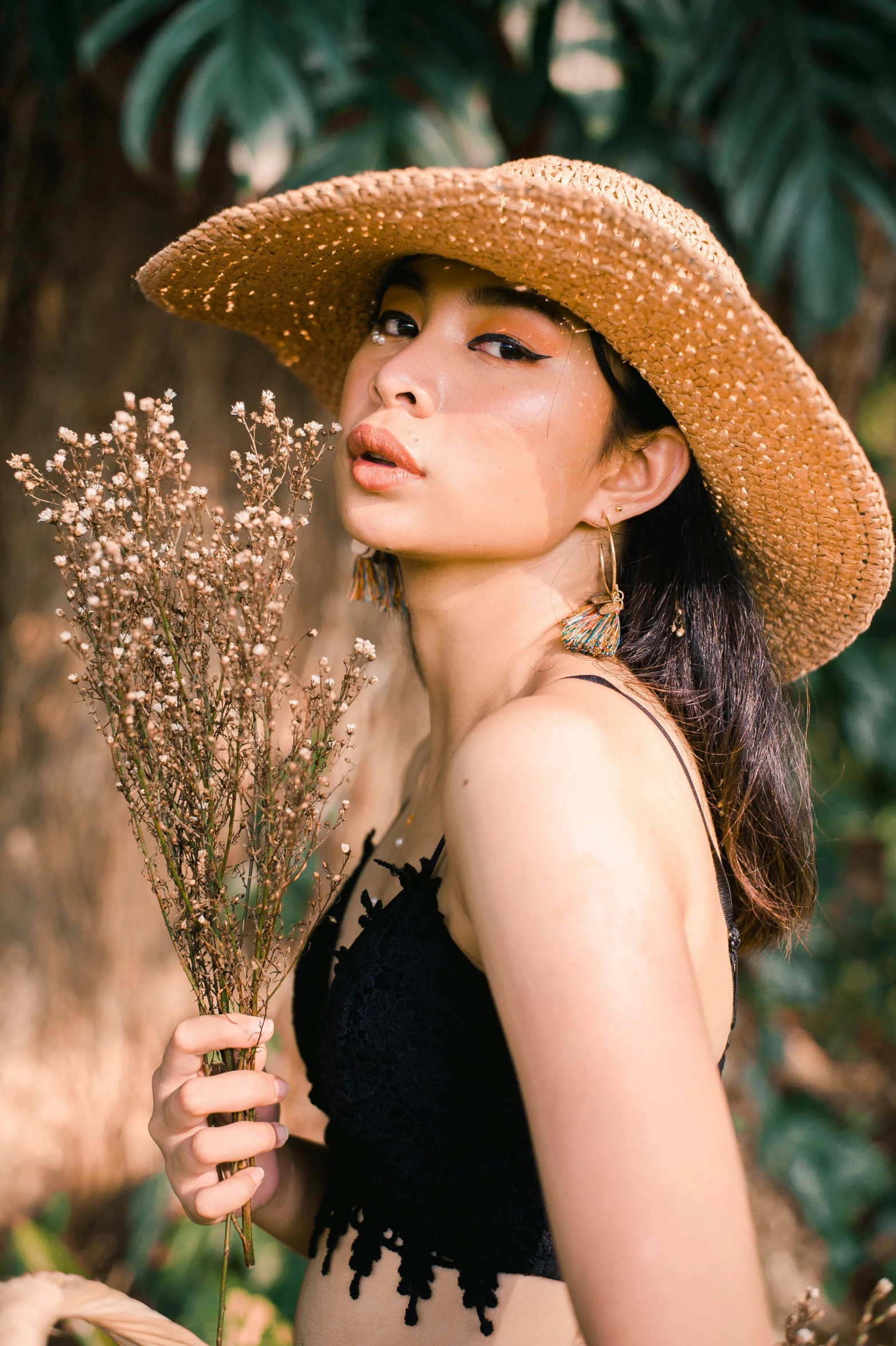 woman wearing hat holding a plant in an outdoor area