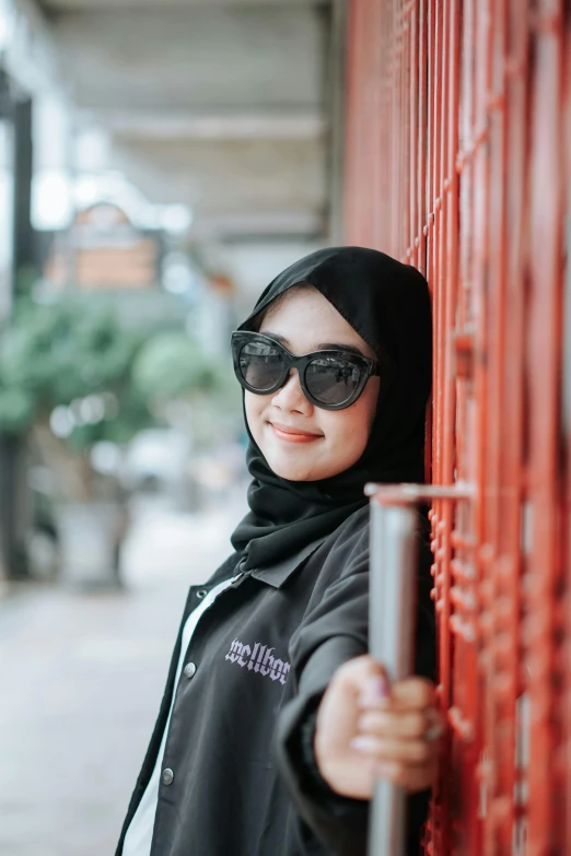 a woman in black coat and sunglasses leaning on wall