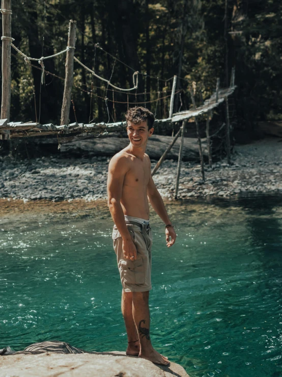 a shirtless man in shorts stands in a shallow pool