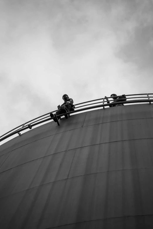 a man sits on a balcony railing over the top of an industrial building