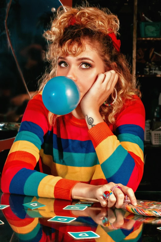 a woman wearing a colorful sweater blowing a blue balloon