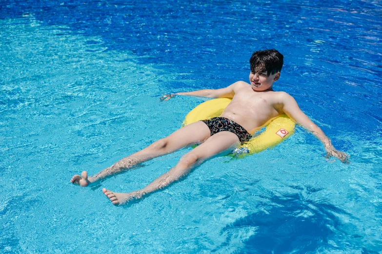 a man in swim trunks laying on a yellow raft in the pool