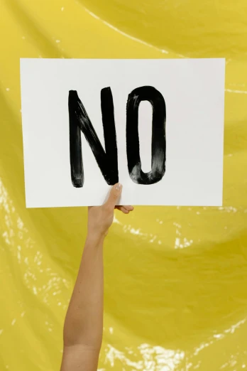 a hand holds up a sign with the word no