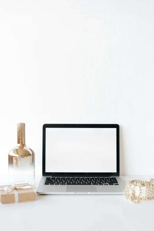 a laptop computer next to a bottle and gold bow on a desk