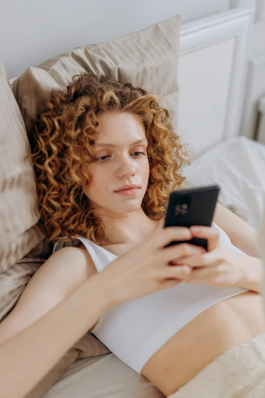 a woman laying in bed looking at a cell phone