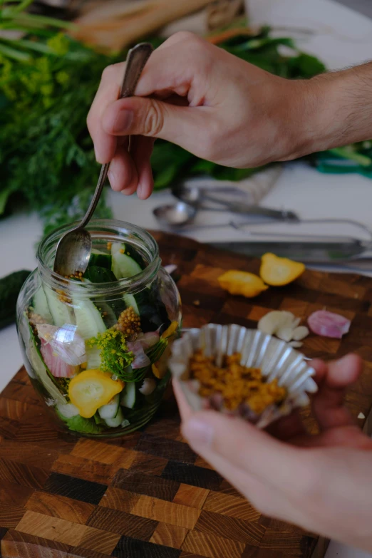 person using spoon to pick up vegetable in a jar