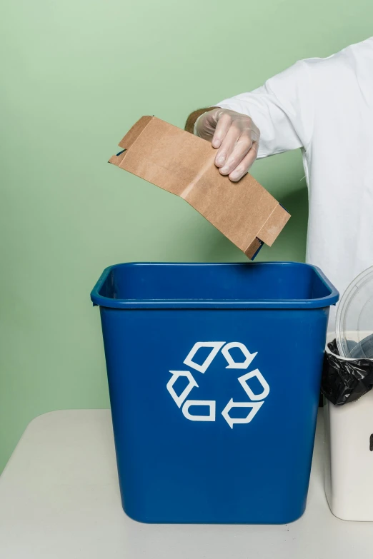 someone in white gloves putting a brown paper on top of the trash can