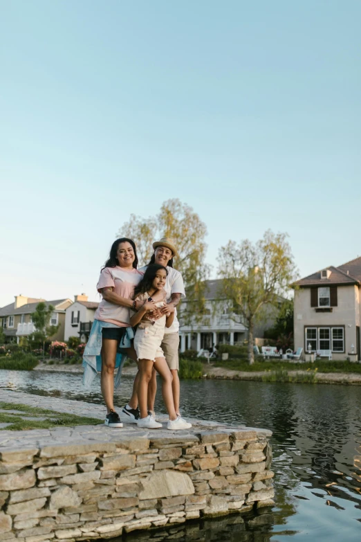 a family posing by a lake in front of some houses