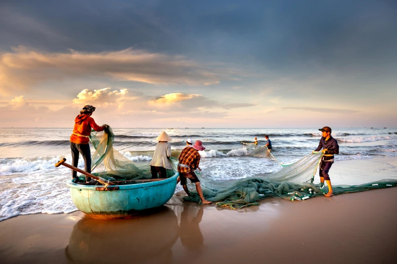 four people are standing on the beach near a boat and fishing nets