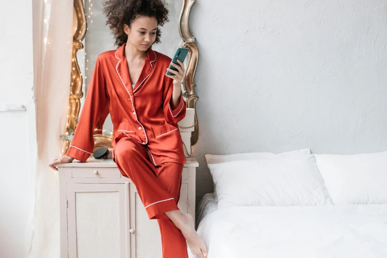 a woman in red pajamas sitting next to a bed with a mirror