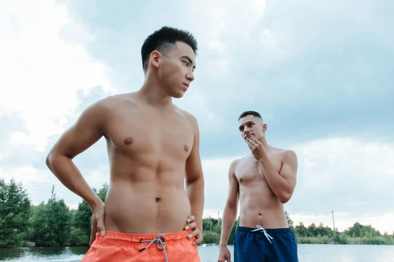 two people in swim trunks posing on the side of a river