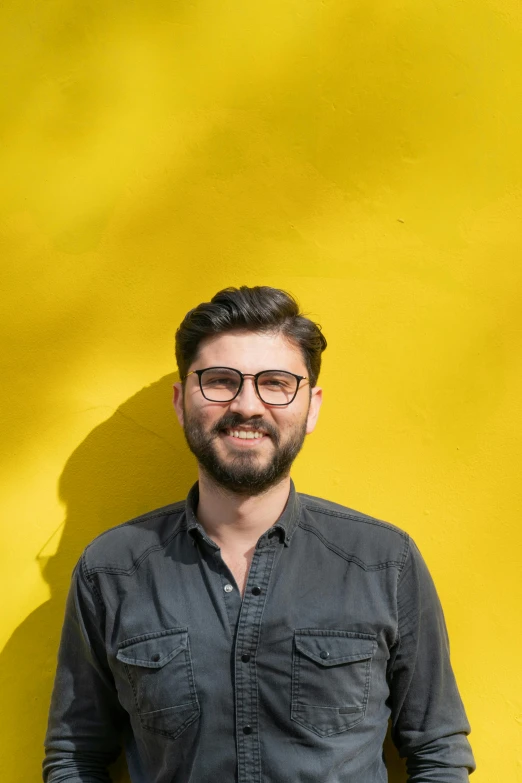 a man poses for the camera in front of a yellow wall