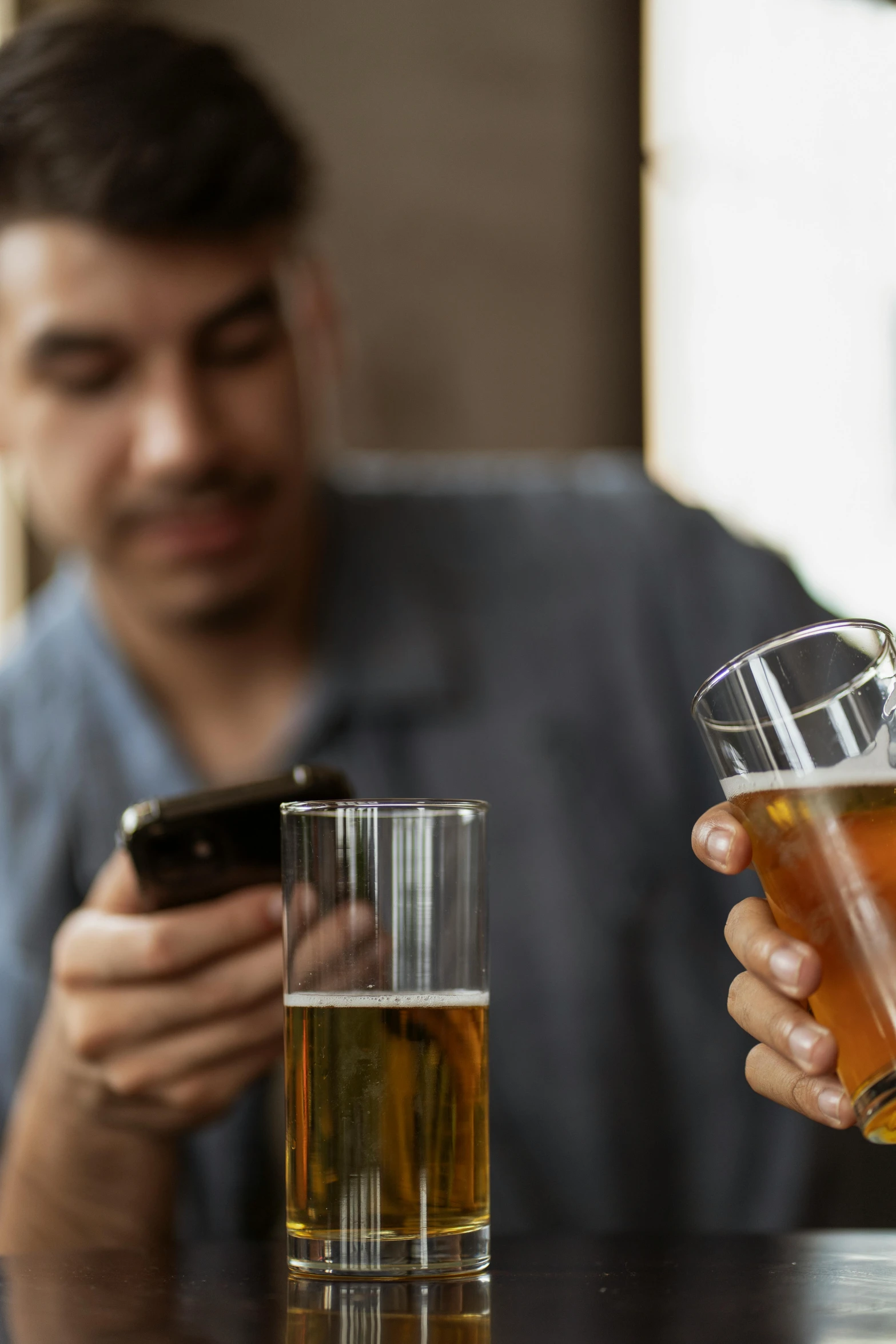 a man is on his cell phone, and he is holding a drink next to two glasses