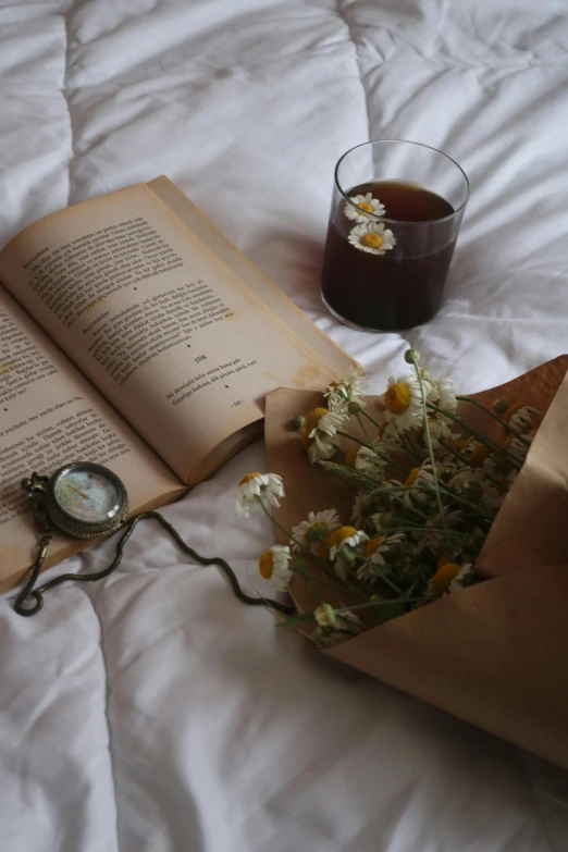 a book laying on top of a bed next to a vase with flowers