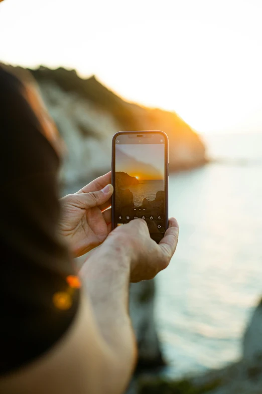 person taking a po on their cell phone in front of a scenic cliff