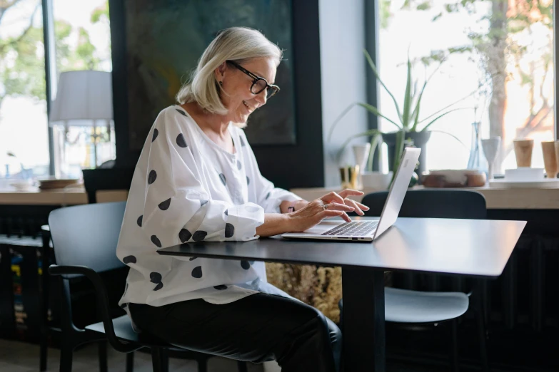 an old woman typing on her laptop in a cafe