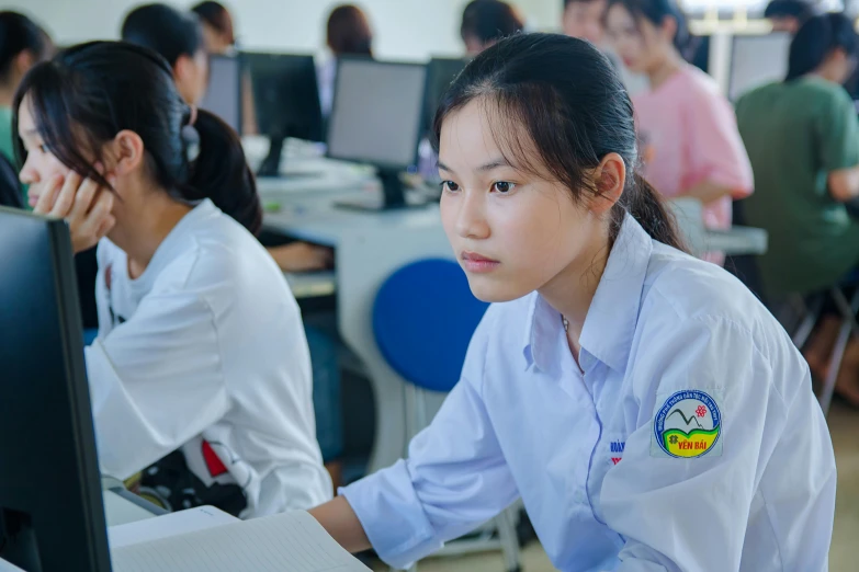 two young women in uniforms using computers at desk