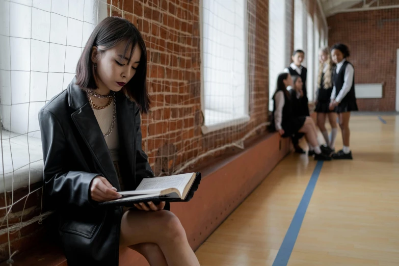 a girl in black coat sitting on ledge reading book