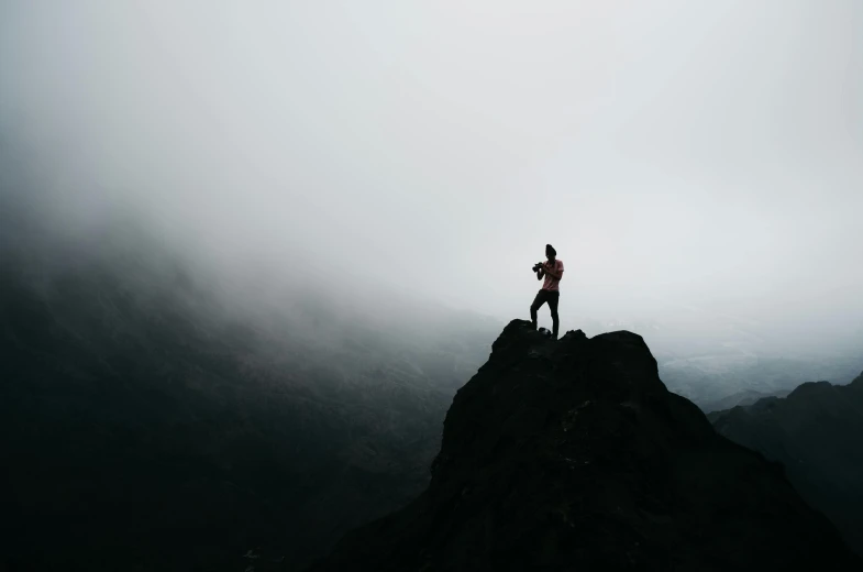 the silhouette of a person stands atop a rocky peak