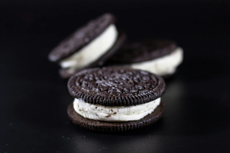 two oreo cookies, one half dipped with cream, sit on a black surface