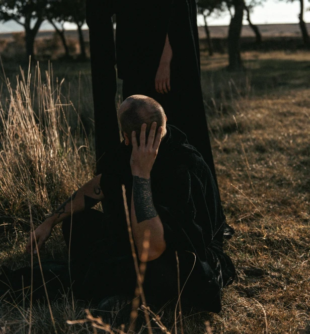 man sitting in field touching the tree with his hands