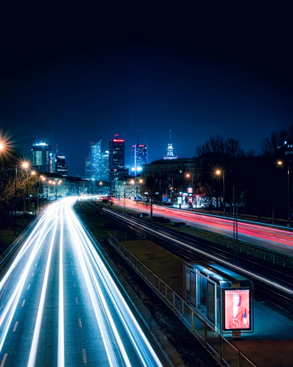 a street with lights trails and buildings in the distance