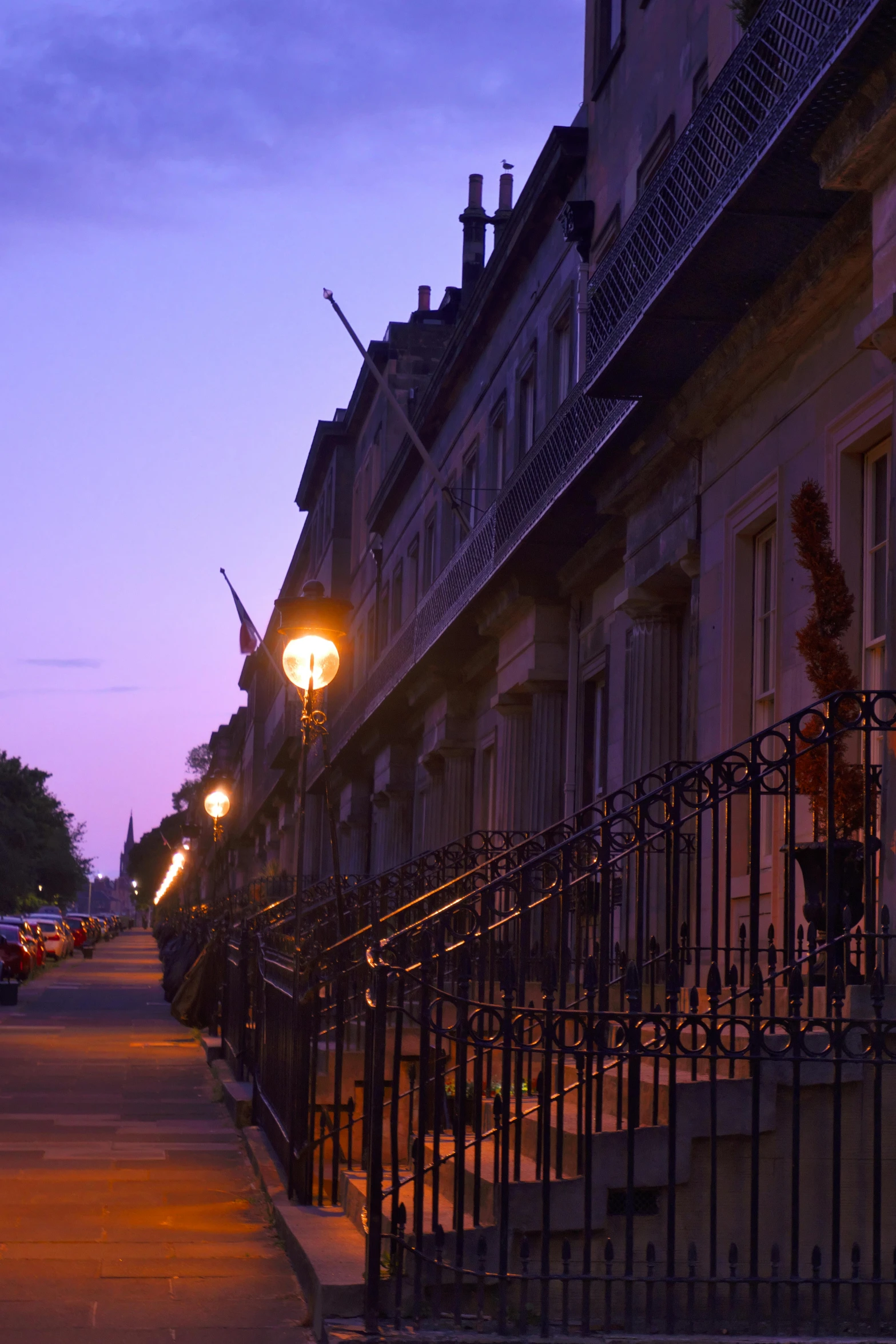 row of older buildings at dusk next to sidewalk with street lamp on it