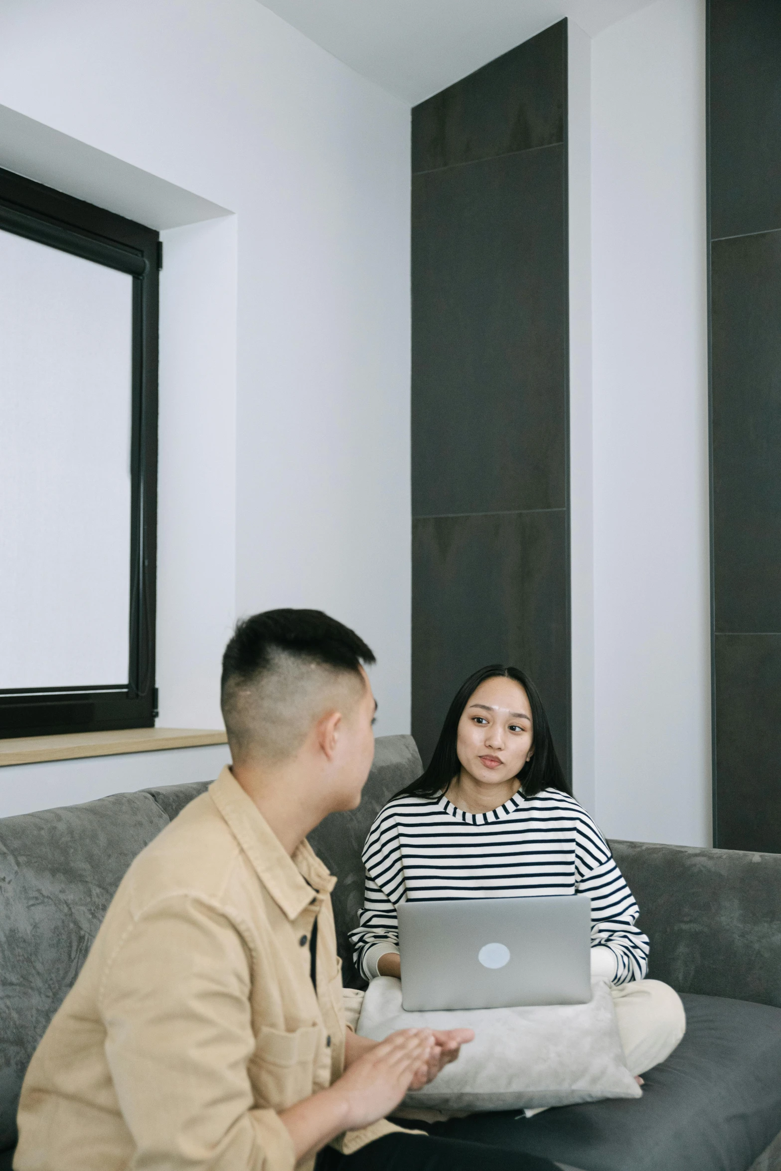 a couple is sitting on the couch talking while looking at their laptop