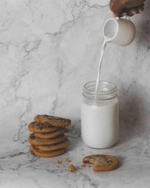 person pouring milk into glass jar with cookies next to it