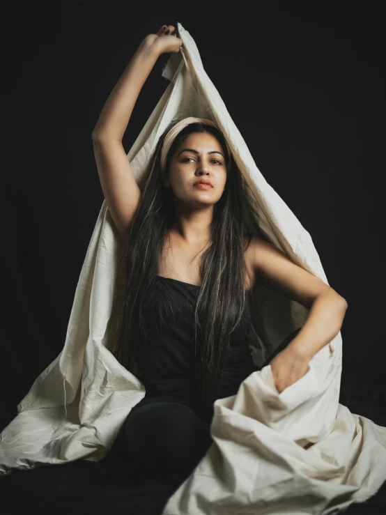 a woman is sitting underneath a white blanket