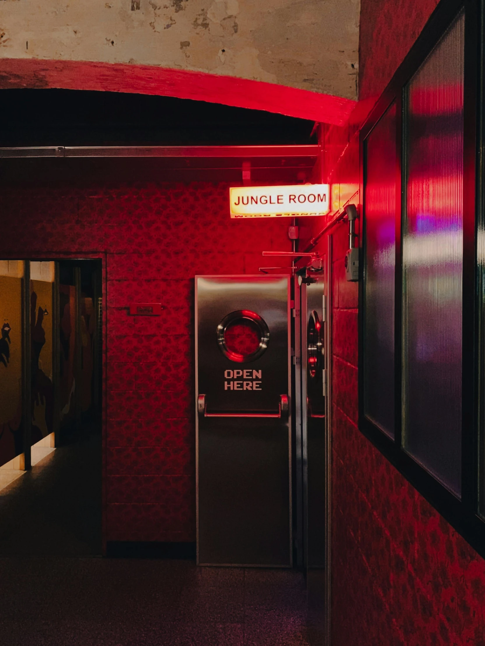 a red lit bathroom that has an open door and closed sign