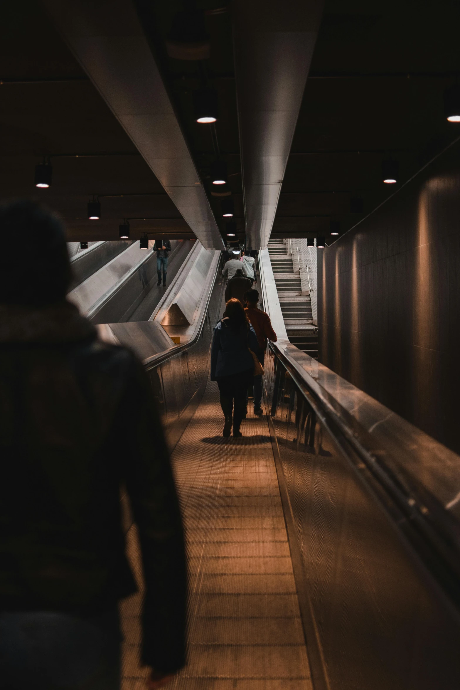 some people are walking up an escalator while one person is on his cell phone