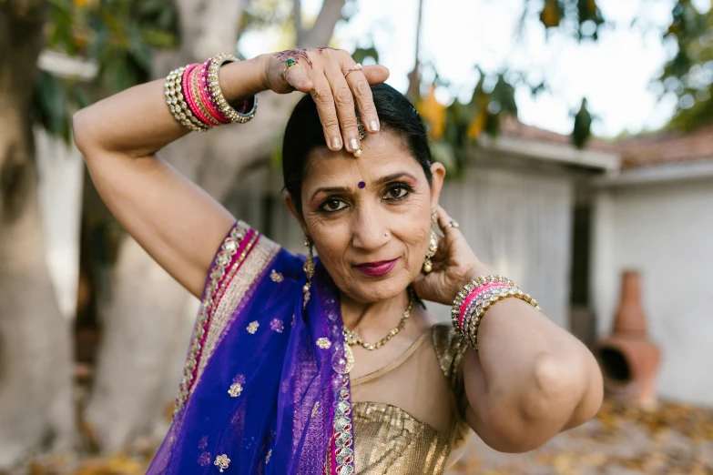 a woman wearing gold and blue saree holding her hands on her head