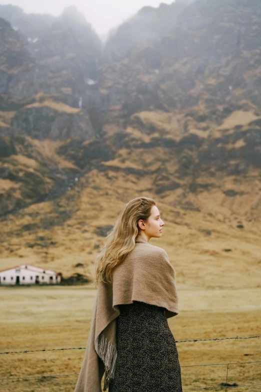 a woman standing next to a fence in front of a mountain