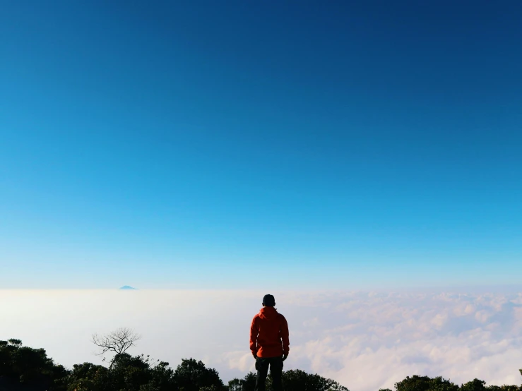 a man in red jacket looking over a cloud covered mountain