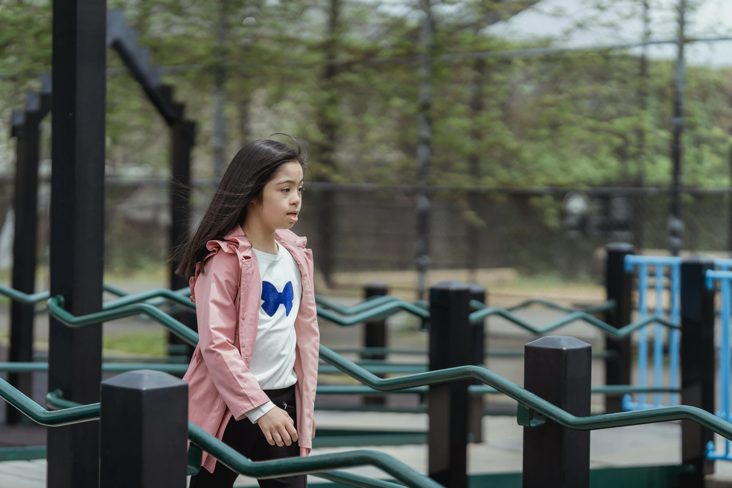 the little girl in the pink jacket stands in front of a metal hand rail