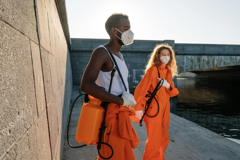 two people in orange jumpsuits, one wearing a surgical mask