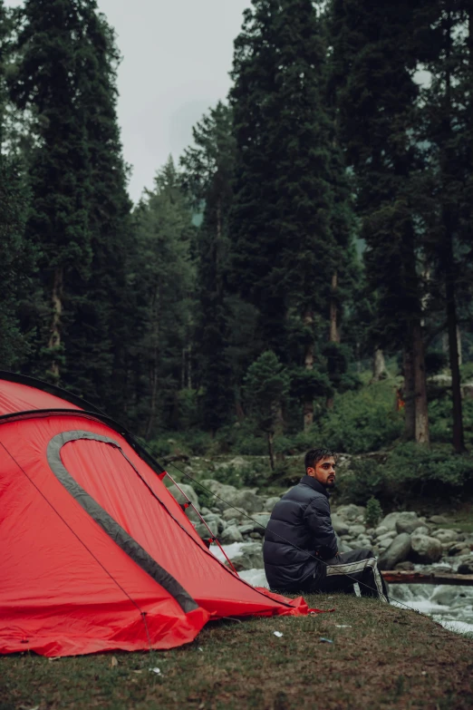 a man sitting in front of a red tent next to trees