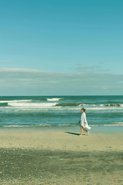 a woman walking across a sandy beach next to the ocean