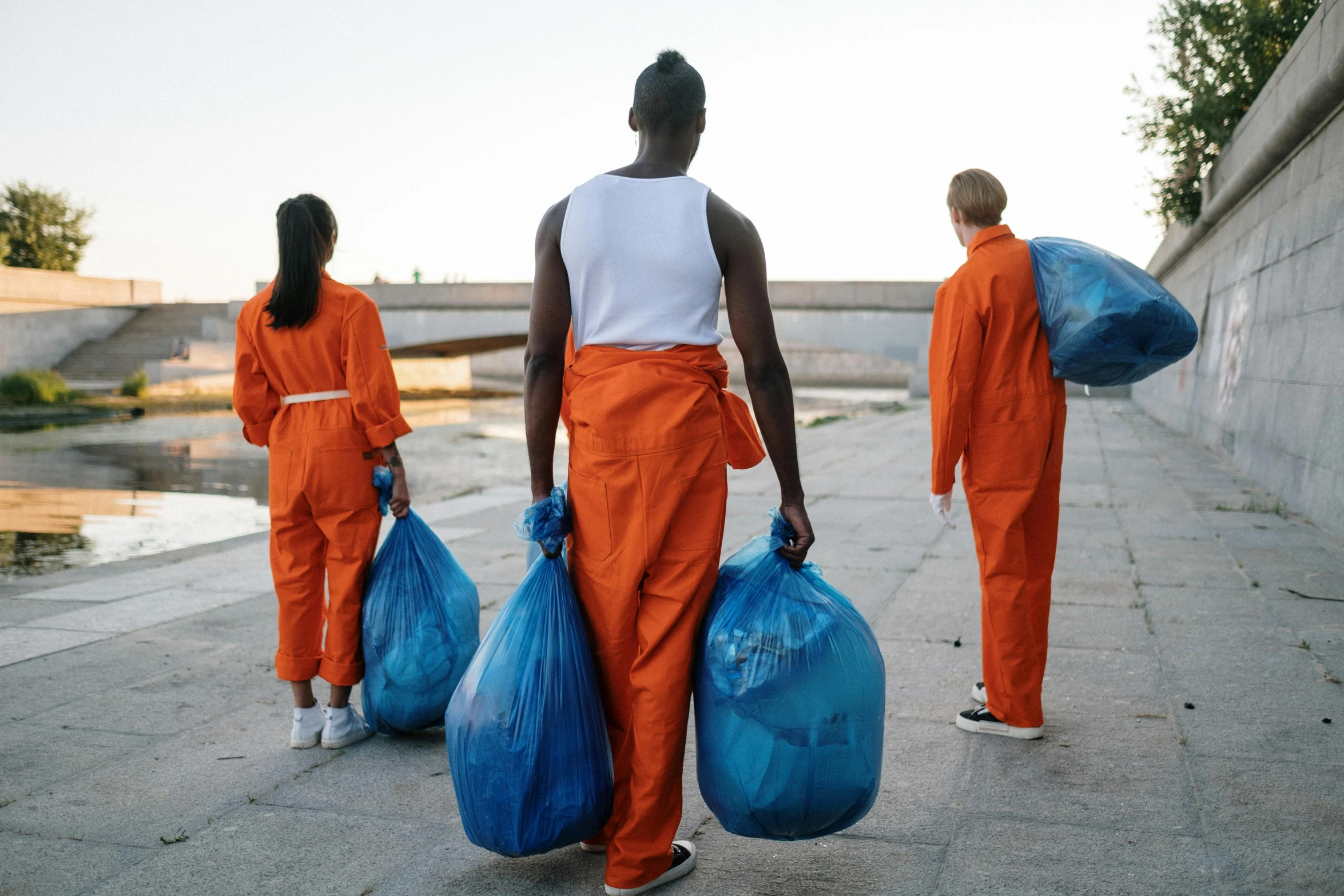 three people walk with orange jumpsuits and bags