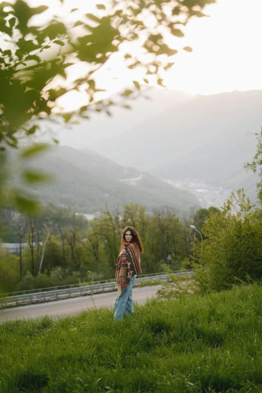 a woman is standing outside on grass and mountains