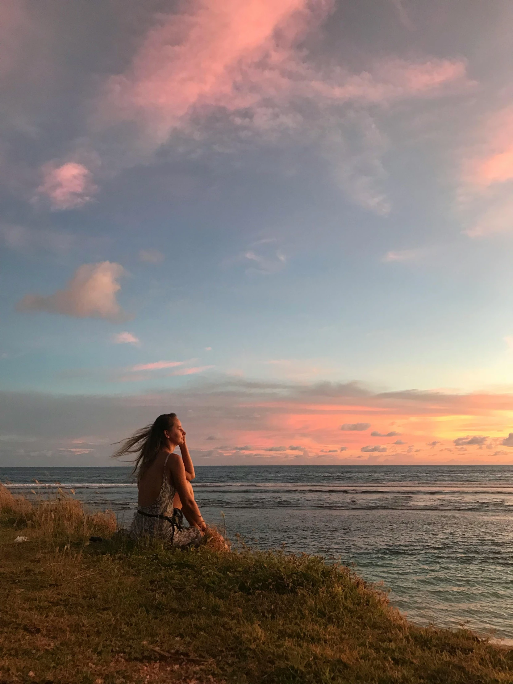 a woman standing on top of a grass covered field near the ocean