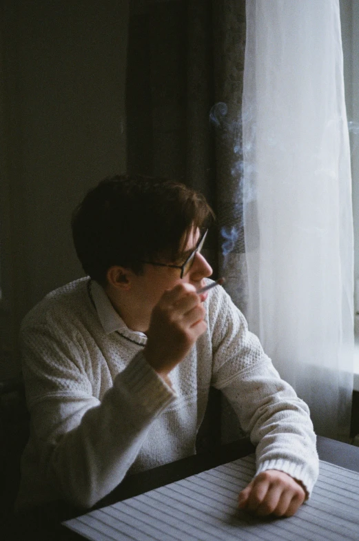 man with glasses sitting down writing on an open laptop