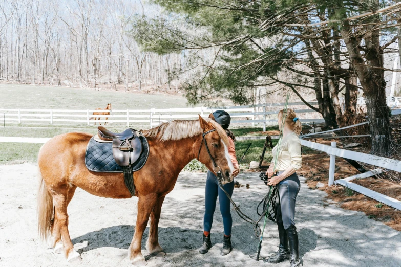 two women stand in the dirt with a horse