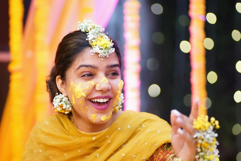 a woman in a yellow sari and flower hairpiece smiles for the camera