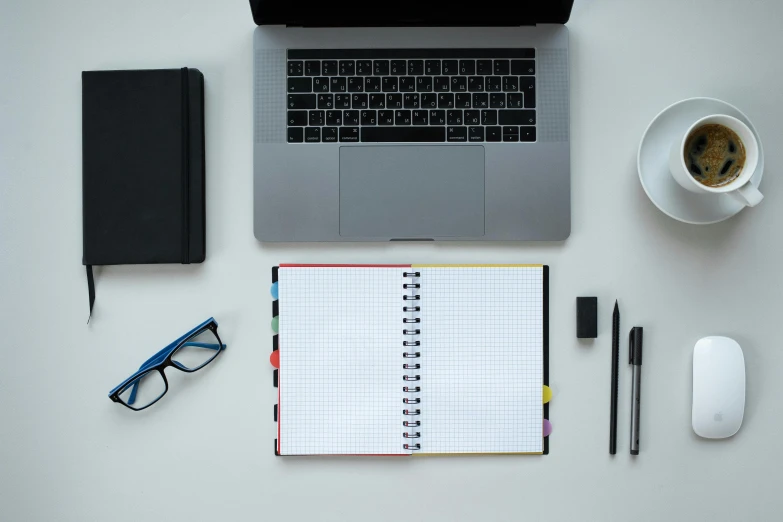 an open planner and coffee cup sitting next to a laptop