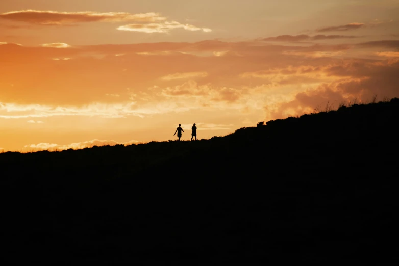 two people on a hill with the sun in the distance